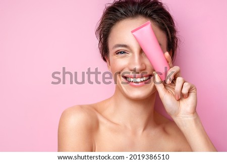 Smiling woman holds tube with cosmetic cream. Photo of attractive woman with perfect makeup on pink background. Beauty concept Royalty-Free Stock Photo #2019386510