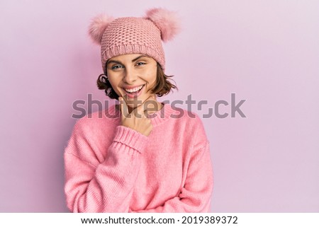 Young brunette woman wearing cute wool cap looking confident at the camera smiling with crossed arms and hand raised on chin. thinking positive. 
