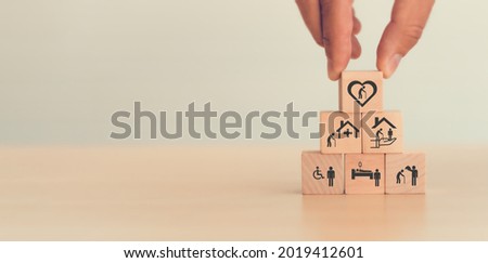 Elderly care concept. Hand holds wooden cubes with icons related to elderly care, medical, rehabilitation service, nursing care for enhancing quality of life in elder people. Used banner, brochure.