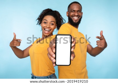 Use this new application. Cheerful black couple pointing at smartphone with blank screen, recommending mobile app, advertising your website, mockup for design. Selective focus Royalty-Free Stock Photo #2019419210