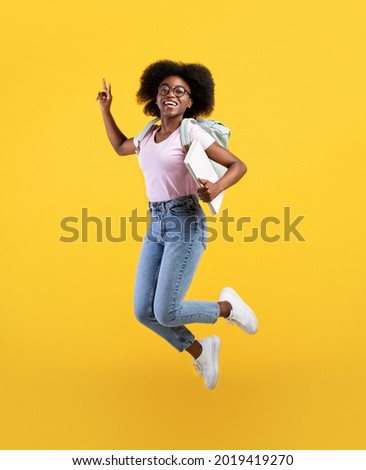 Enjoying student life. Full length portrait of african american lady jumping, wearing backpack and holding notepads over yellow studio background, crop Royalty-Free Stock Photo #2019419270