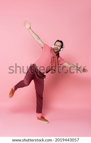 Man in headphones singing and dancing on pink background