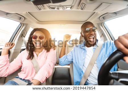 Summer Holidays And Roadtrip Concept. Front view portrait of excited black couple in sunglasses driving car, dancing to music and singing favorite song, going on vacation for rest and relax, sun flare Royalty-Free Stock Photo #2019447854