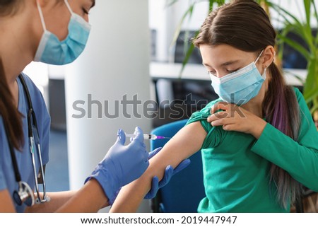 Clinical trial for new modern Covid vaccine during global pandemic. Little girl in medical face mask getting injection at hospital. Doctor or nurse giving shot to female patient with syringe Royalty-Free Stock Photo #2019447947