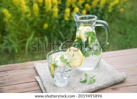 A jug and a glass with homemade lemonade on a wooden background.
