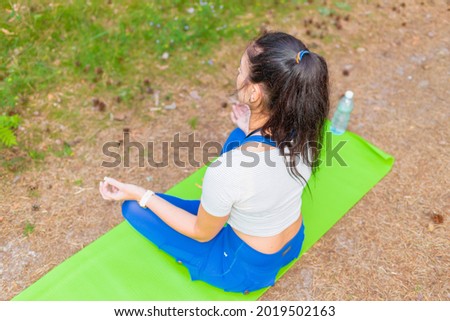 Young attractive female meditate in park.Young female relaxes in yoga pose in green summer warm nature