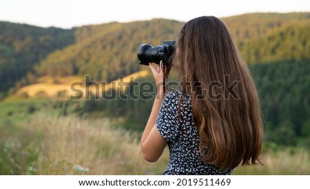Anonymous and unrecognizable girl with a camera. Learning photography for young people and adolescents. Landscape of hills in the mountains of southern France on a sunny summer evening.