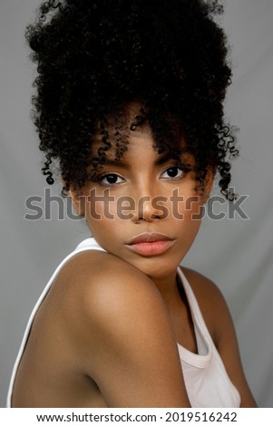 Curly hair woman looking at camera on gray background for editorial and makeup