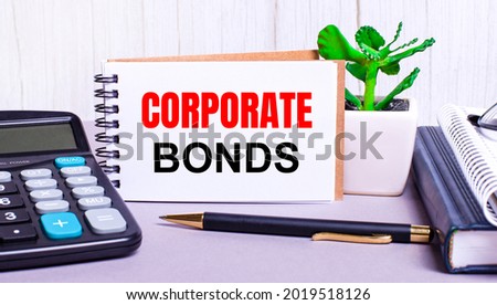On the desktop are a calculator, diaries, a potted plant, a pen and a notebook with the text CORPORATE BONDS. Business concept. Workplace close up