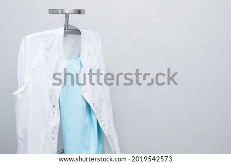 Medical white coat on a metal stand against the background of a white wall.