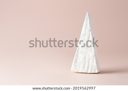 A triangular piece of soft cheese with white brie mold. On a light pink pastel background.