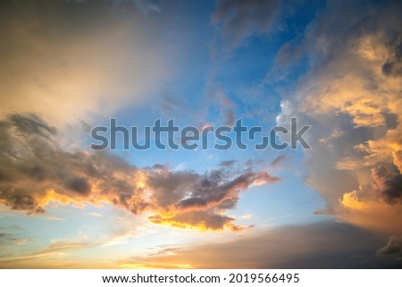 Dramatic sunset landscape picture with puffy clouds lit by orange setting sun and blue sky.