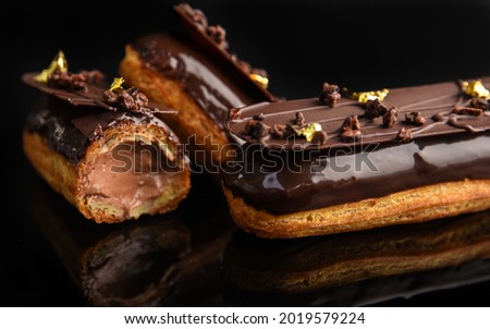 Eclair stuffed in chocolate on a black background. Royalty-Free Stock Photo #2019579224