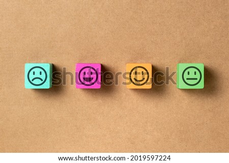 Emoticon faces in colors wooden blocks over brown paper. Service evaluation and satisfaction survey concepts. Angry, neutral, good mood and happy. Copy space.