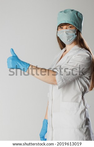 Woman with a medical mask and hands in latex glove shows the thumb up. Love our medical professionals. Protection against coronavirus. Woman doctor wearing medical mask encourages vaccination