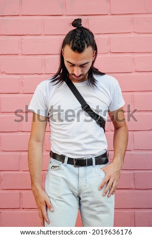 young hispanic latino man with long hair with a braid, fashionable looking down, pink wallpaper, vertical picture