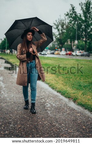Young beautiful woman holding a blacks umbrella and enjoying a walk in the park during rain