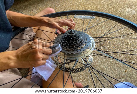 Asian rider take care of the sport bike wheel with clean cloth( seclective focus),  young man cleaning the bicycle wheel inside in the summer day.