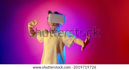Cute girl teenager using VR glasses over colorful neon background with blank space for text.