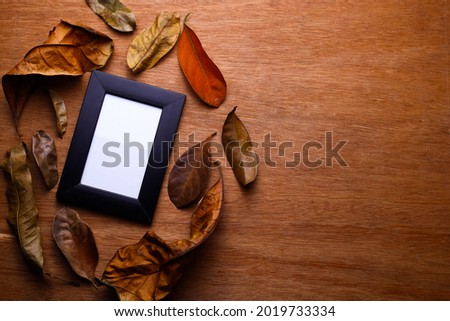 Top view.
Black photo frame in the circle of dry leaves on wooden table with space for text.