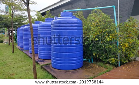 Rows of blue water tanks. Plastic buckets back up water on the cement floor behind a public restroom with copy space.