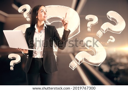 Attractive young european businesswoman with laptop pointing up in blurry office interior with abstract questions. Question and solution concept. Double exposure