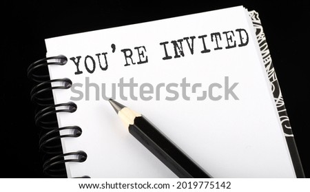 YOU'RE INVITED written text in small notebook on a black background