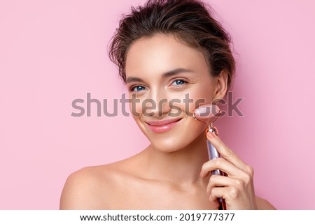 Beautiful woman using stone facial roller. Photo of woman with perfect skin on pink background. Beauty and skin care concept