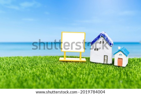 Miniature vintage style house with blank sign on green grass over blurred beach background, real estate and property business concept, hosue for sale, property investment