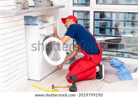 male adult repairman with tool and clipboard checking washing machine in bathroom