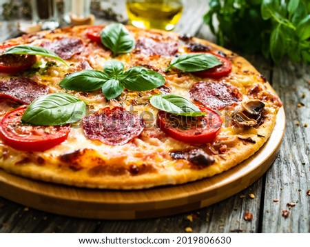 Circle pepperoni pizza with mozzarella, salami and tomatoes on wooden table
