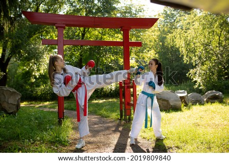 Two purposeful woman fighting using karate technique kick and punch martial arts outdoors at front of traditional Japanese gate . Couple young women wearing in white kimono training karate martial 