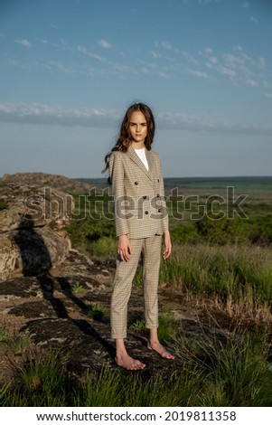 girl in a suit, naturalness, big stones, blue sky, in motion, naturalness, suit in natural shades