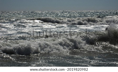 Beautiful blue sea waves with white foam close up. Bustling, violent ocean and horizon in background with cloudy, stormy sky. Minimalistic picture of sea landscape.