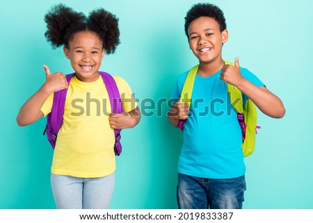 Portrait of two nice cheerful kids going back to primary school showing thumbup isolated over bright teal turquoise color background