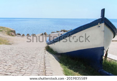 A picture of an old white and blue boat in front of the shiny blue sea