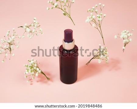 Unbranded brown cosmetic spray bottle and flying gypsophila flowers on pink background. Natural organic spa cosmetics. Body mist, Mockup, template.