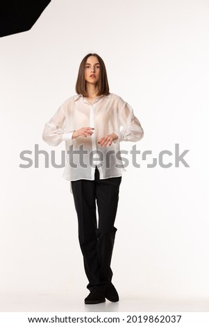 Girl wear black classic pants, and white shirt. Fashion studio portrait of young elegant woman. Fashion portrait, look book and catalogue style. Woman looks proud and arrogant.