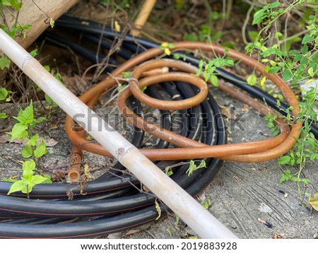 The hose is made from rubber which is a product of petroleum chemistry. Hoses and cables are piled together on the ground in the garden. A hose is a type of gardening device used for watering plants. 