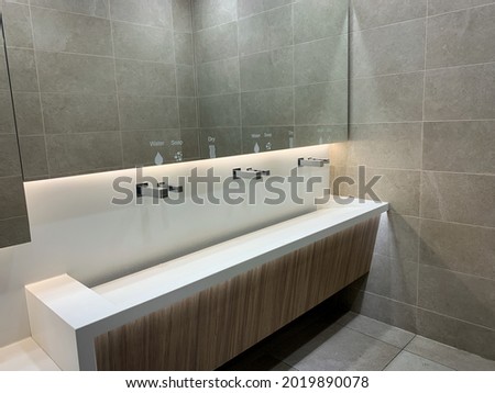Modern white sink with big mirror and abstract metal faucet with water, soap and dry signs over it in a contemporary public toilet.