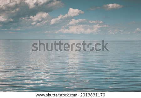 The minimalist seaside landscape and a beautiful blue sky full of curly clouds above that reflect the water's surface.