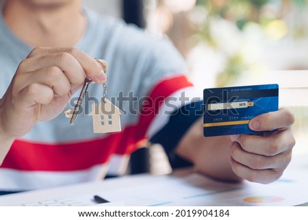 Man holding keys house with house shaped keychain and mockup credit card on wooden table.Real estate concept for buying a new home.