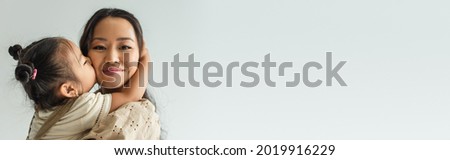 asian toddler girl kissing cheek of happy mother isolated on grey, banner
