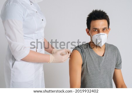 Studio shot of young man in face mask giving injection vaccine against coronavirus during vaccination on isolated white background. Nurse using syringe to inject vaccine to male patient.
