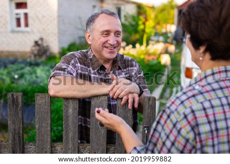 neighbors middle aged man and woman chatting near the fence in the village Royalty-Free Stock Photo #2019959882