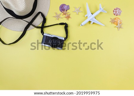 Top view or flat lay of camera, straw hat, airplane model with sea shells and starfish on yellow background with copy space. Summer beach vacation background.
