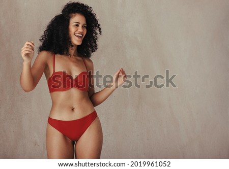 Happy young black woman celebrating her natural body. Body positive and confident young woman smiling cheerfully while wearing red underwear against a studio background.