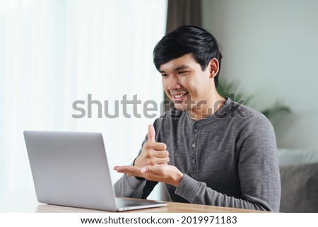 Young Asian man deaf disabled using laptop computer for online video conference call learning and communicating in sign language.
