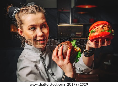 young woman chef with two burger in hands on dark background in cafe