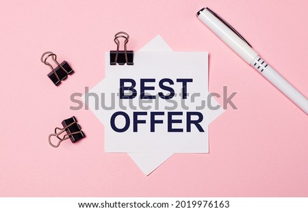 On a light pink background, black paper clips, a white pen and white note paper with the text BEST OFFER. Flat lay